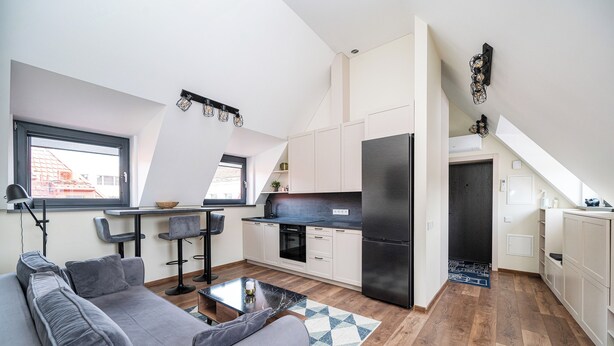 A modern kitchen with white cabinets, a black refrigerator, and a dining area with a gray sofa and a coffee table.