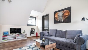 A modern living room with a grey sofa, a coffee table, a TV, and a bookshelf.