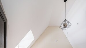 A bedroom with a sloped ceiling, a desk, a chair, a bed with a headboard, and a hanging light fixture.