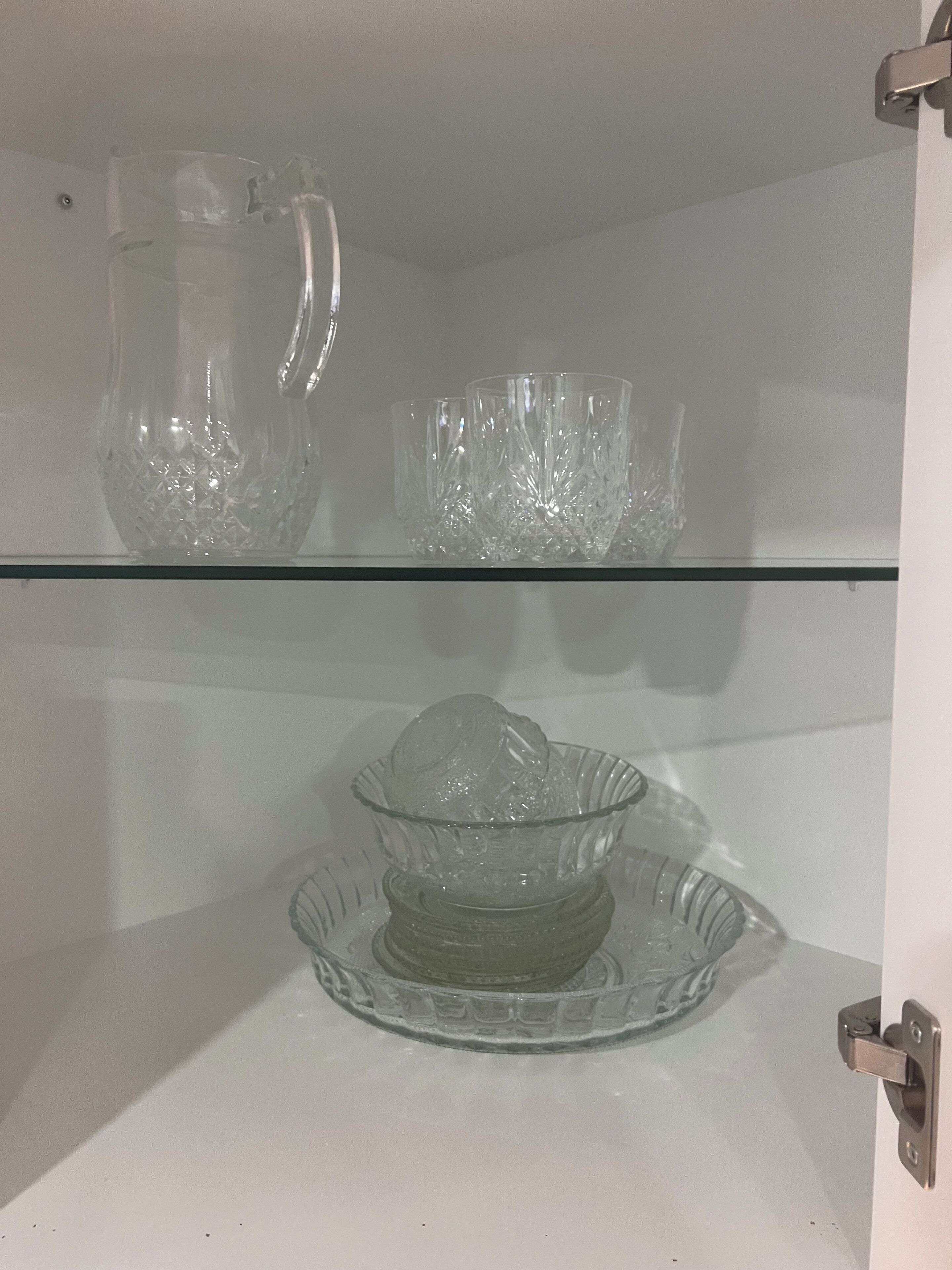 A glass display cabinet with a pitcher, multiple glass cups, and a glass bowl.