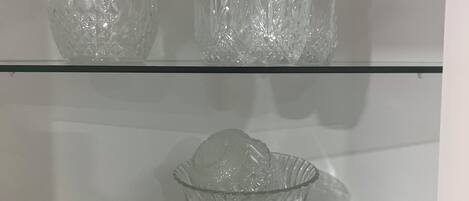 A glass display cabinet with a pitcher, multiple glass cups, and a glass bowl.