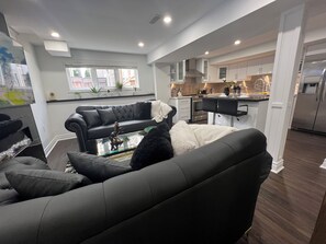 A modern living room with a black leather sofa, a glass coffee table, and a kitchen in the background. - Guest suite in Ajax/Toronto (Ajax)