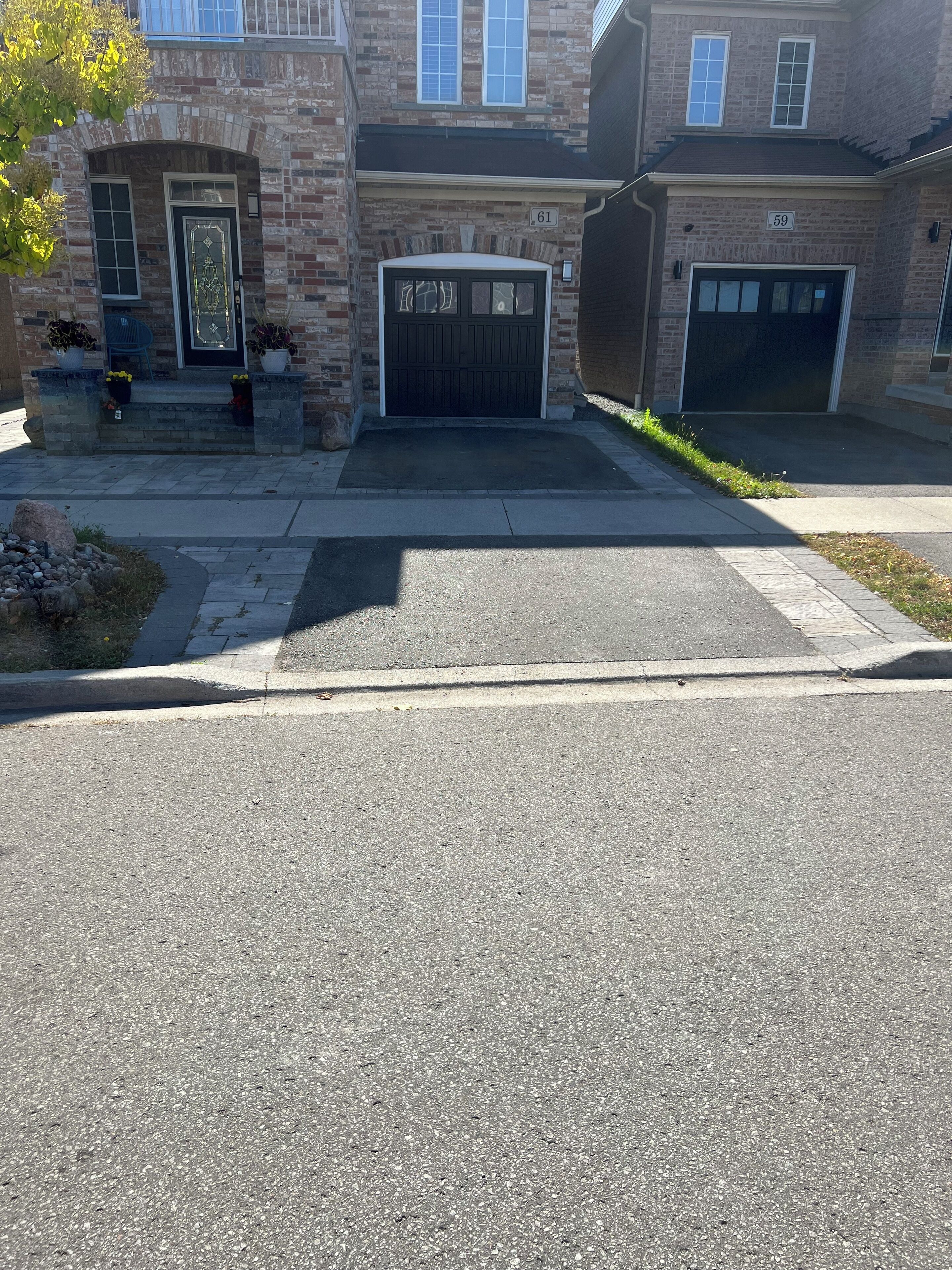 A residential street with a brick house, numbered 61, featuring a garage and a front door.