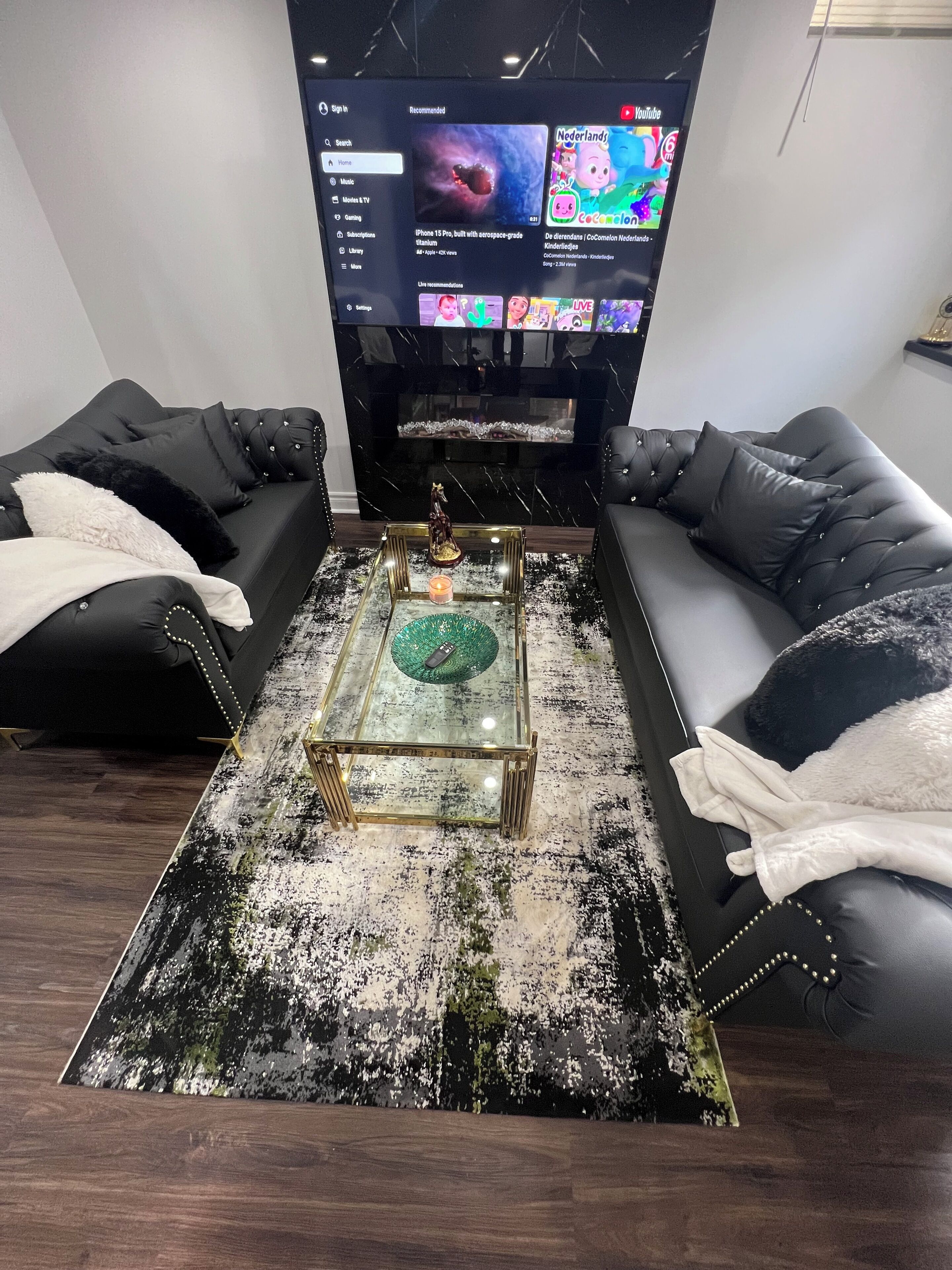 A modern living room with a black leather sofa, a glass coffee table, and a flat-screen TV mounted on the wall.