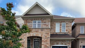 A two-story house with a stone facade, a front porch, and a garage. - Warm & Stylish 4BR Home | 3BA • Near Toronto (Ajax)