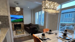 A modern dining area with a wooden table, black and orange chairs, and a chandelier. - Warm & Stylish 4BR Home | 3BA • Near Toronto (Ajax)