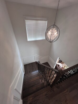 A staircase with dark wooden steps and metal railings, a hanging light fixture, and a window with blinds.
