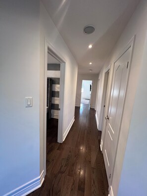 A hallway with wooden flooring, white walls, and a door leading to another room.