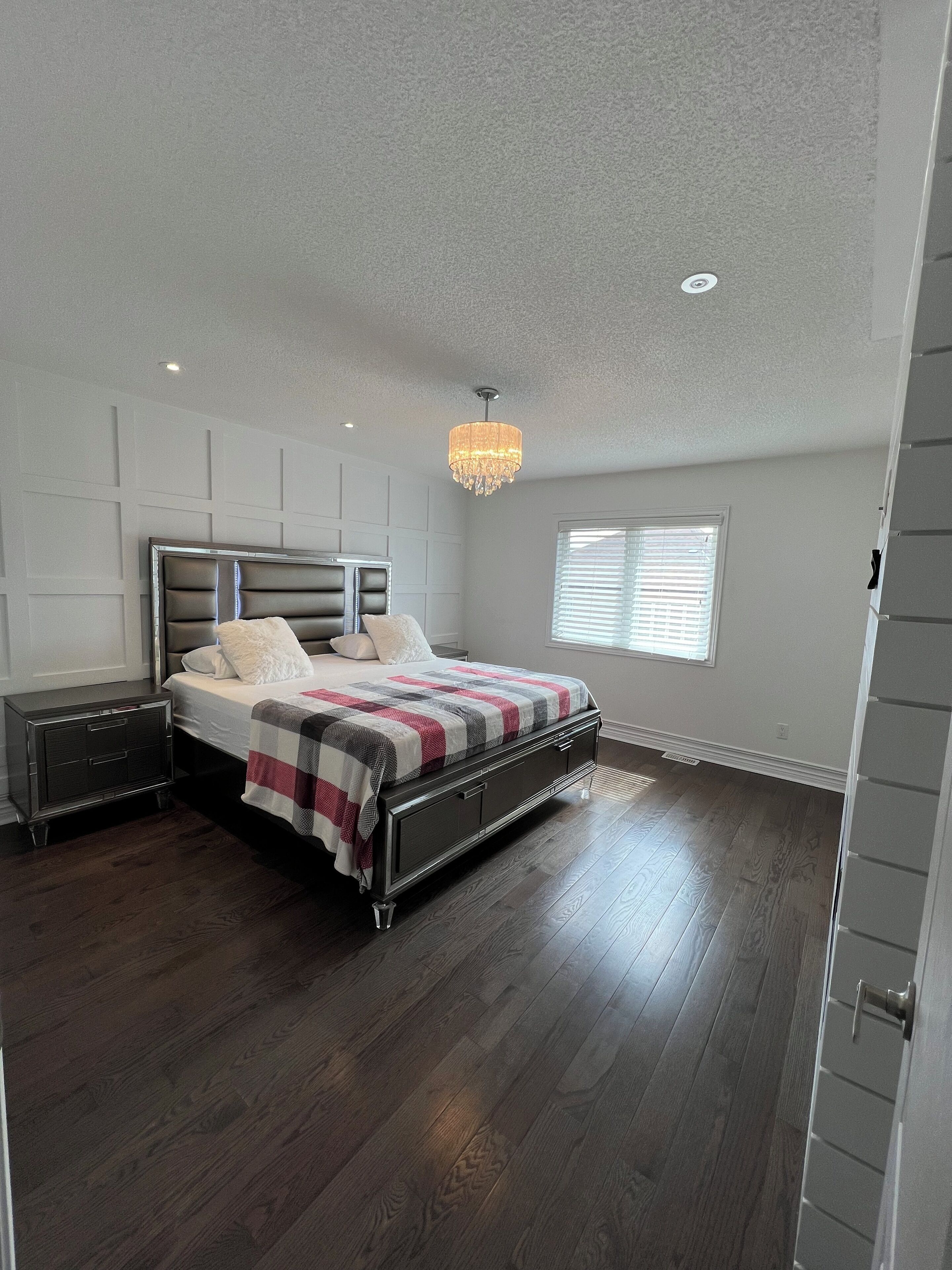 A bedroom with a bed, bedside tables, a chandelier, and a window.