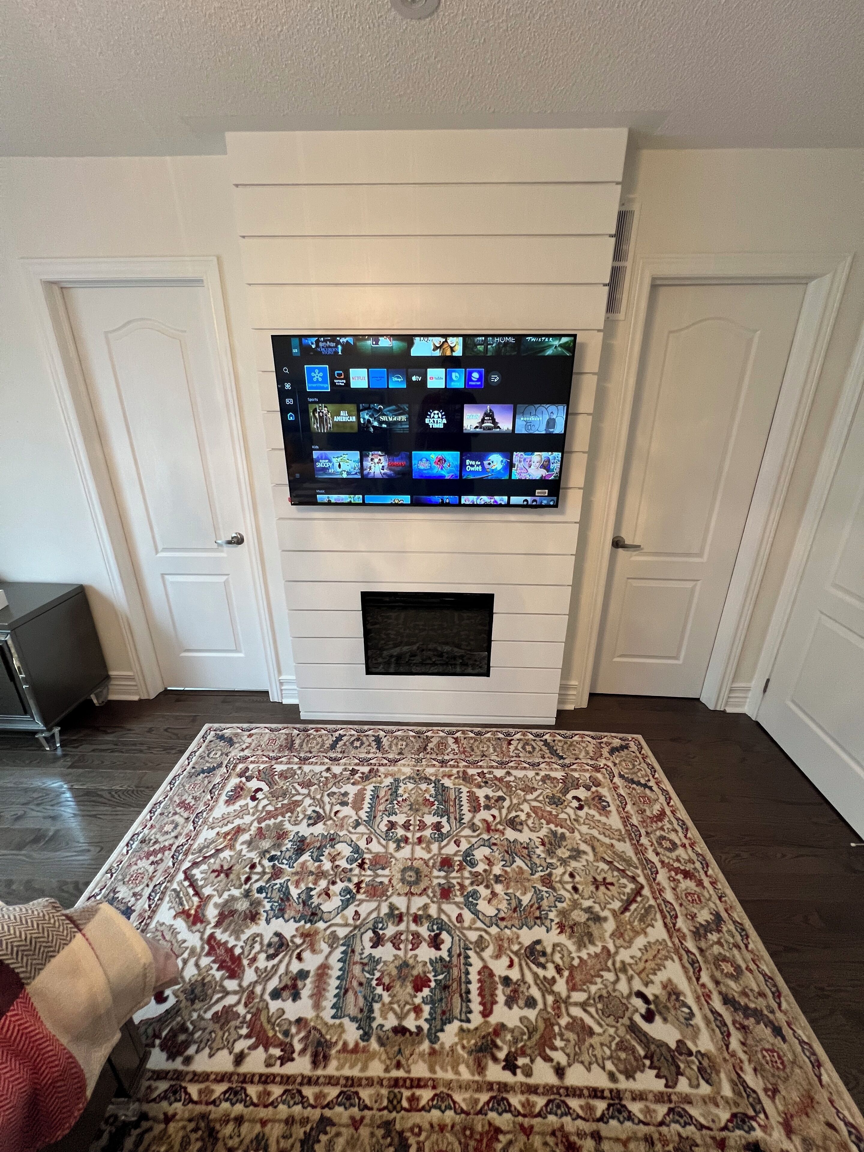 Una sala de estar con un televisor de pantalla plana sobre la chimenea, un tapete estampado en el suelo y un piso de madera oscura.