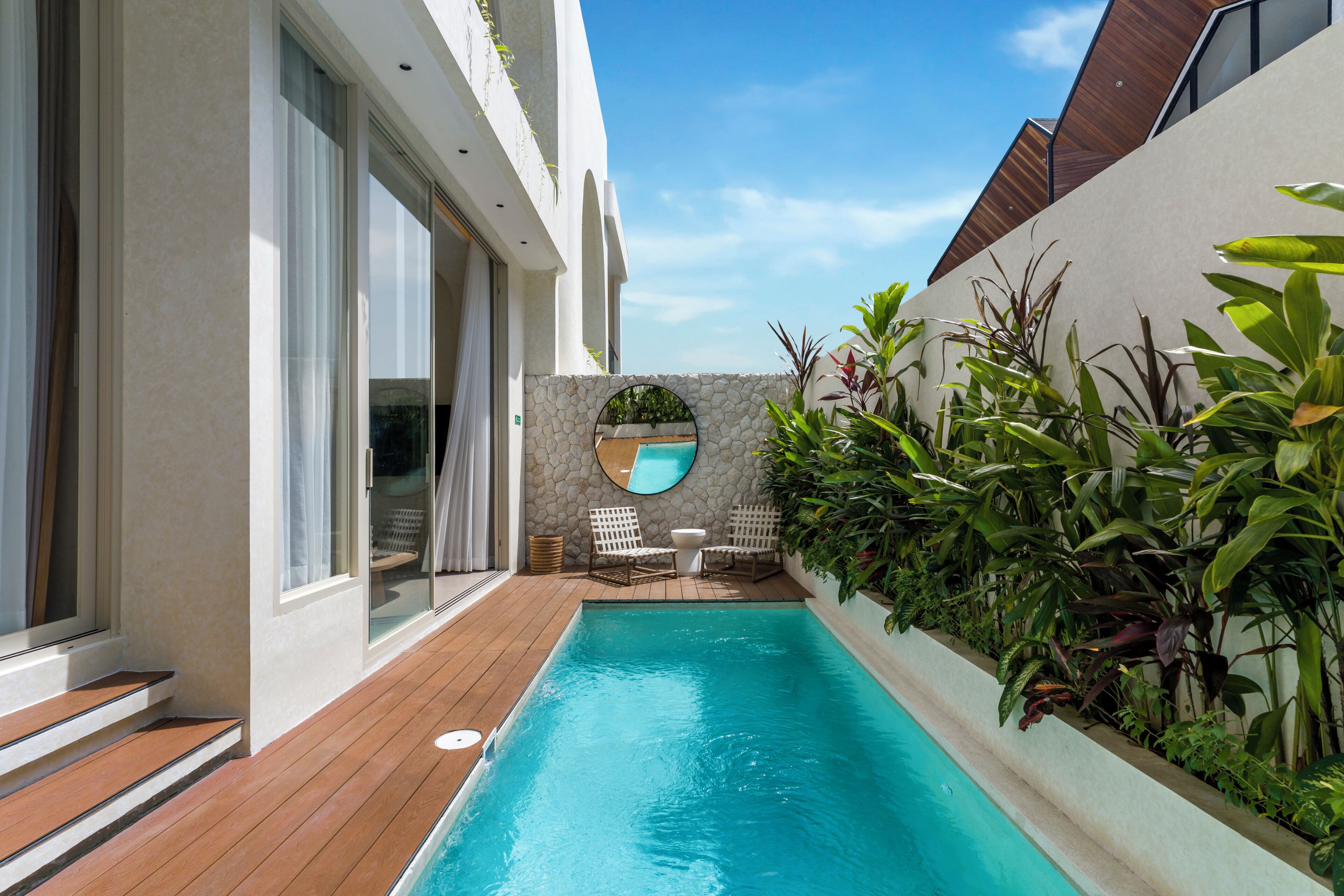 Ein moderner Poolbereich mit Holzterrasse, Steinmauer und einem runden Spiegel.