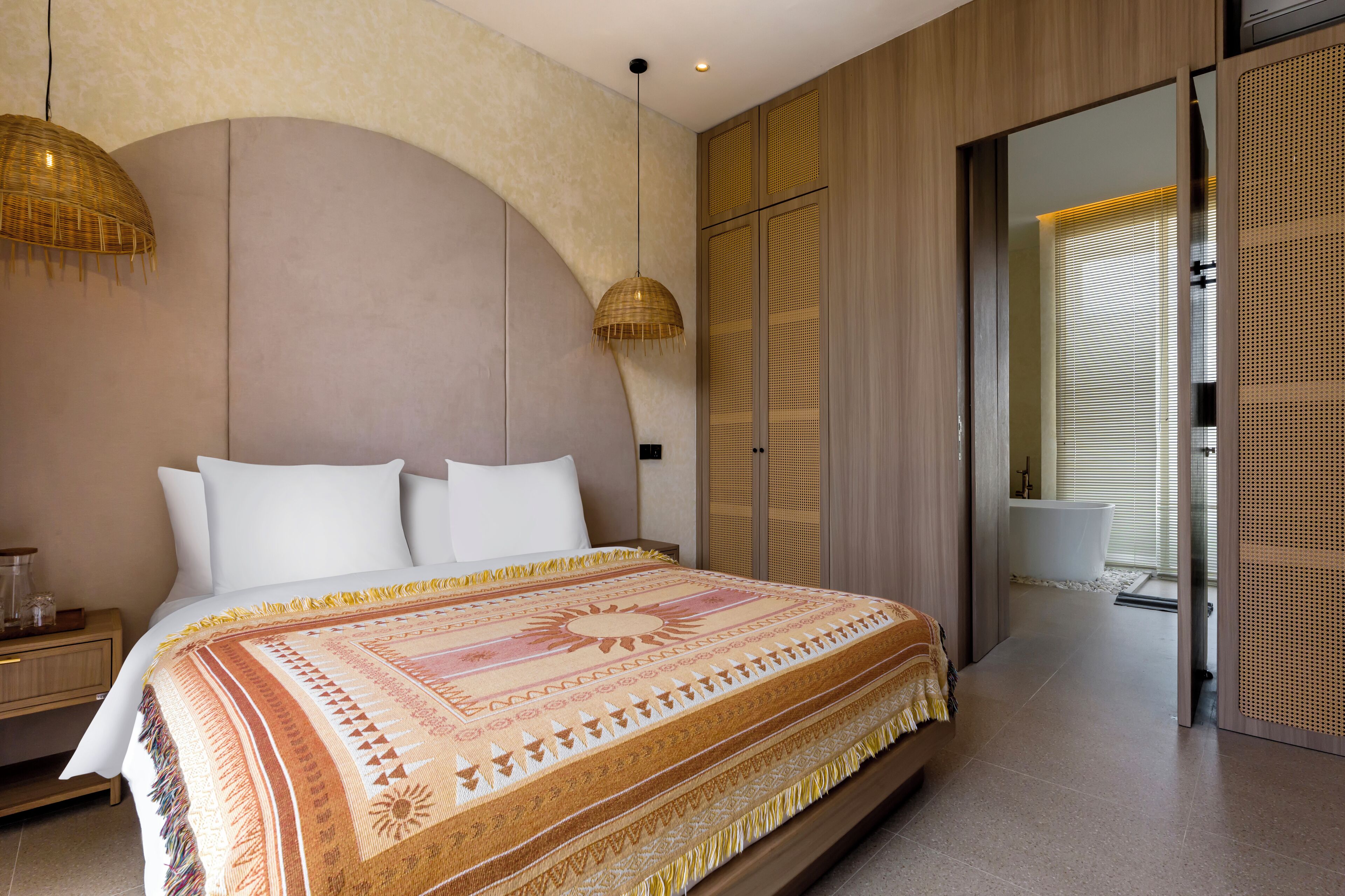 A bedroom with a large bed, a bedside table, a hanging lamp, and a view of the bathroom.