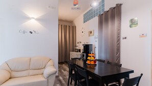 Ein modernes Wohnzimmer mit einer Couch, einem Esstisch mit Stühlen, einer Kaffeemaschine und einer Wanduhr.