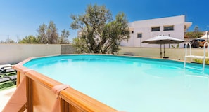 Una piscina con un pontile in legno, un ombrellone bianco e un edificio sullo sfondo.