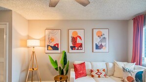 A modern living room with a white sofa, a floor lamp, and abstract wall art. - Downtown Mesa Apartment - Pool, W/D, 65” TV, Walk to Dining (Mesa)