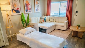A modern living room with a sofa, a bed, a lamp, and artwork on the wall. - Downtown Mesa Apartment - Pool, W/D, 65” TV, Walk to Dining (Mesa)