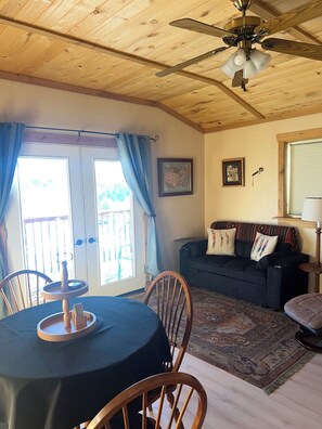 A cozy room with a wooden ceiling, a ceiling fan, a dining table with chairs, a sofa with cushions, and a patterned rug. - Chrome Bear Ranch Guest House (Montrose)
