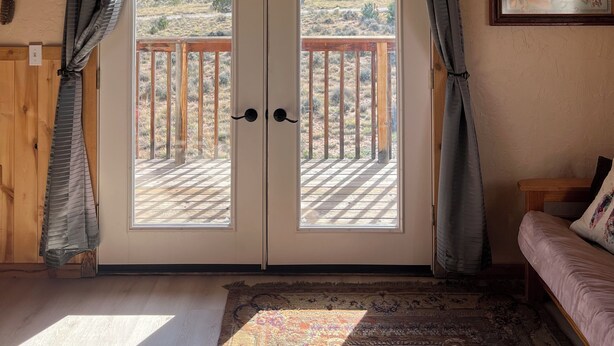 Ein Zimmer mit Holzboden, einem Deckenventilator, einem großen Fenster mit Vorhängen, Blick auf eine Terrasse und einer an der Wand hängenden Karte.