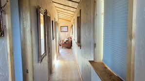 Ein langer Flur mit Holzwänden und -decke, der zu einem Zimmer mit einem Bett und einem Fenster führt.