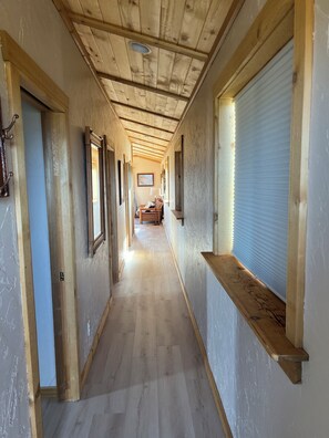 A long hallway with wooden walls and ceiling, leading to a room with a bed and a window. - Chrome Bear Ranch Guest House (Montrose)