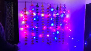 Une pièce dont un mur est décoré d’ornements colorés suspendus et qui possède une fenêtre avec une grille en métal.