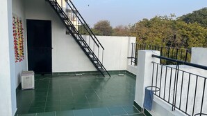 Une terrasse sur le toit, avec un escalier en métal menant à une porte, une poubelle et une serviette bleue suspendue à la rambarde.