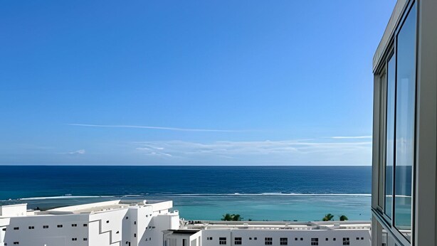 A coastal view with a clear sky, a building with large windows, and a view of the ocean. - OCEAN AND BEACH VIEW ROOFTOP (Boca Chica)