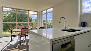 A modern kitchen with a large island, a built-in dishwasher, and a window overlooking a garden. - Designer 6BR Home Backyard Direct Park Access (Auckland)