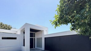 A modern building with a flat roof, a large glass door, and a concrete courtyard. - Designer 6BR Home Backyard Direct Park Access (Auckland)