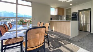 A modern kitchen with a dining area, large windows, and a view of the city. - Designer 6BR Home Backyard Direct Park Access (Auckland)