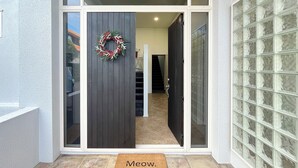 A modern entrance with a glass door, a dark wooden panel, and a doormat with "Meow." - Designer 6BR Home Backyard Direct Park Access (Auckland)