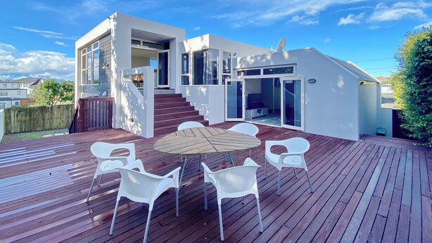 A modern house with a deck, white chairs, and a round table. - Designer 6BR Home Backyard Direct Park Access (Auckland)