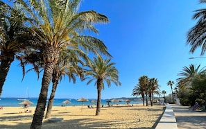 Ein Strand mit Palmen, Sonnenschirmen und blauem Himmel.