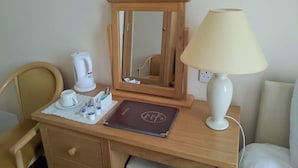 Een houten bureau met een spiegel, een witte lamp, een koffiezetapparaat, een boek en een kop.