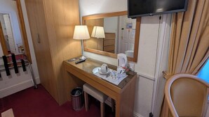 Hotelkamer met een houten bureau, twee lampen, een televisie, een spiegel, een stoel en een kleine prullenbak.