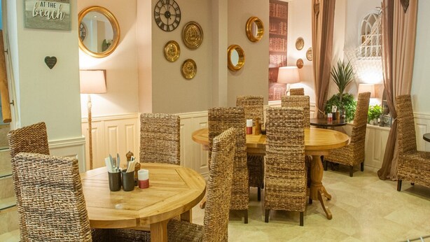 Een eetgedeelte met rieten stoelen, een houten tafel en een ronde spiegel aan de muur.