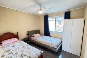 Quarto com duas camas, ventilador de teto, janela com cortinas e guarda-roupa.