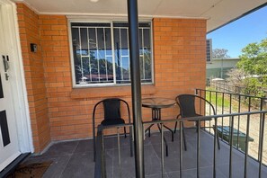 Un balcón con dos sillas y una mesa, una ventana con rejas de metal y un muro de ladrillo.