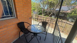 A patio with a round glass table and two chairs, a brick wall, and a metal fence.