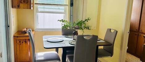 A dining area with a table, chairs, a potted plant, and a window with blinds.