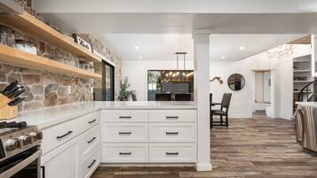 Une cuisine moderne avec des meubles blancs, un mur d’accent en pierre et une cuisinière encastrée.