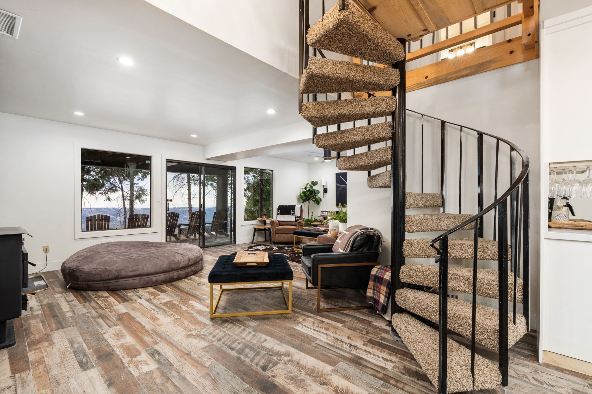 Un salon moderne doté d’un escalier en colimaçon, de grandes fenêtres et d’un coin salon confortable.