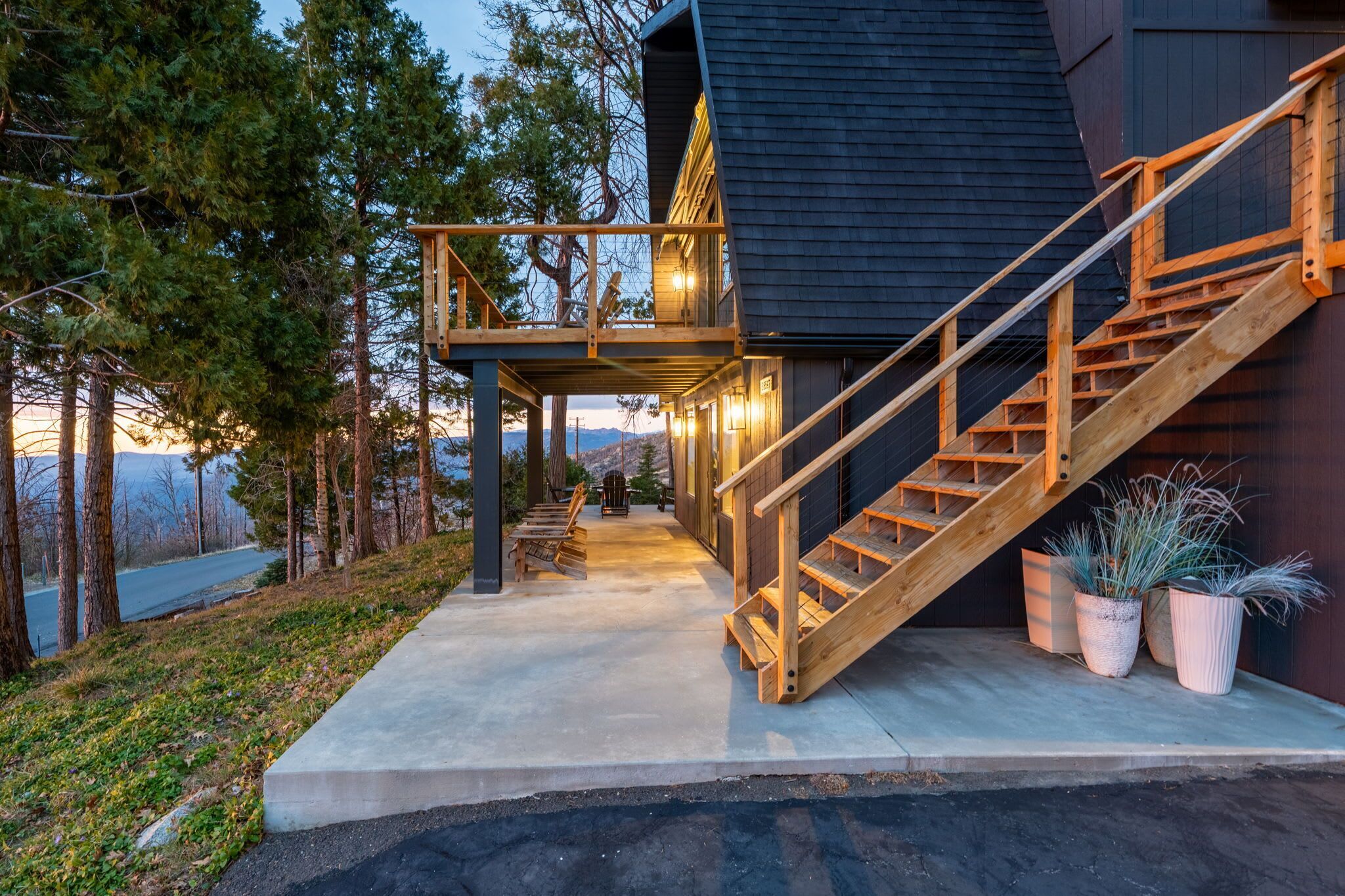 Une maison moderne avec un escalier en bois menant à une terrasse, entourée d’arbres et offrant une vue sur la montagne.