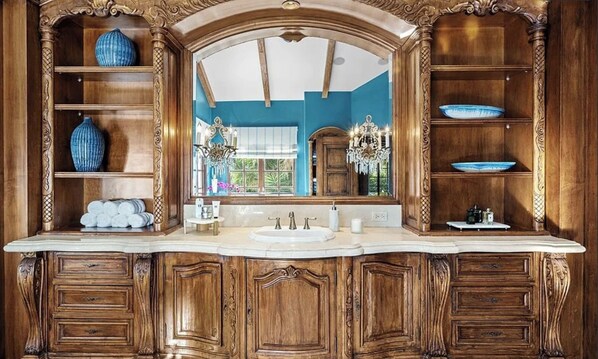 A luxurious bathroom with a large mirror, ornate wood cabinetry, and a vanity with a sink.