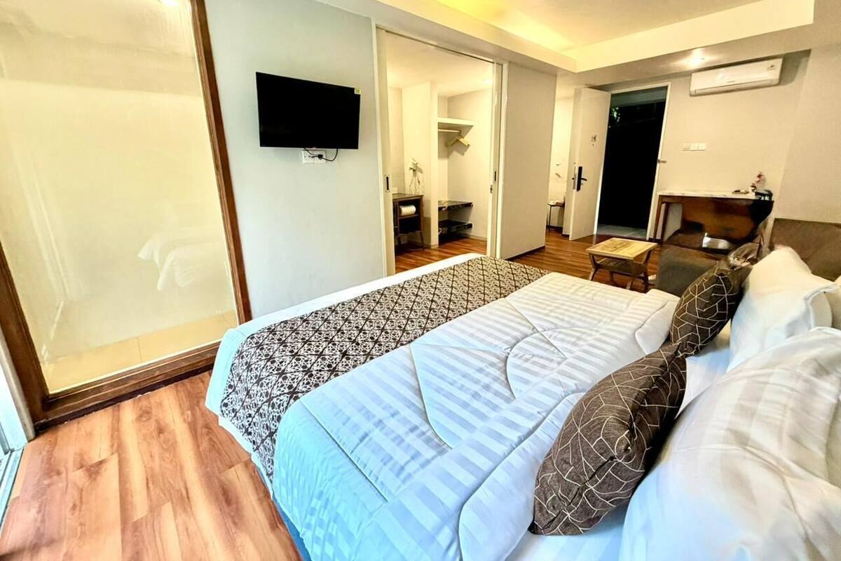A hotel room with a large bed, a TV mounted on the wall, a wooden floor, and a sliding door leading to a bathroom.
