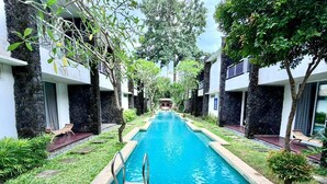 A swimming pool with lounge chairs and a stone wall on one side. - Dealton Hotel Sanur (Denpasar)