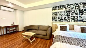A room with a wooden floor, a sofa, a small wooden table, a bed with patterned bedding, and a wall with decorative black and white patterns. - Dealton Hotel Sanur (Denpasar)