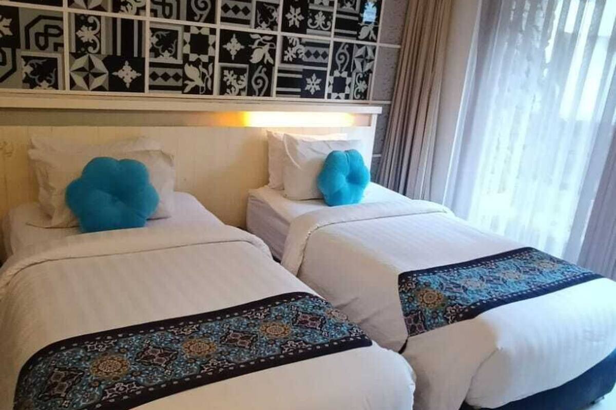 A hotel room with two beds, a decorative wall, and a window with curtains.