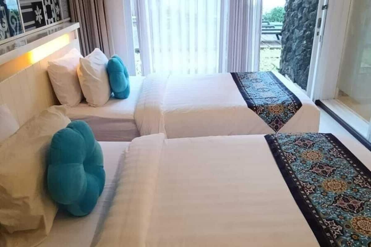 A hotel room with two beds, a large window with curtains, a patterned rug, and a decorative wall.