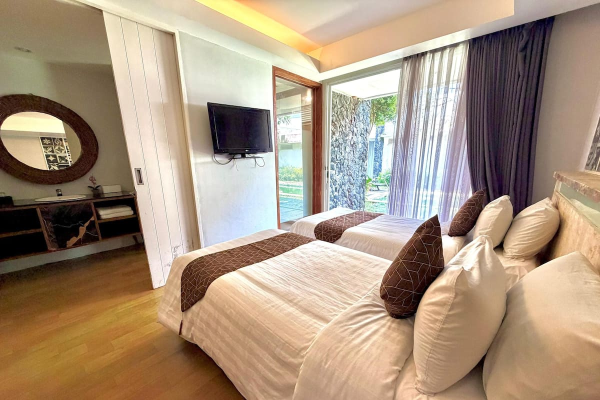 A hotel room with two beds, a TV, a bathroom with a mirror, and a view of the outdoors.